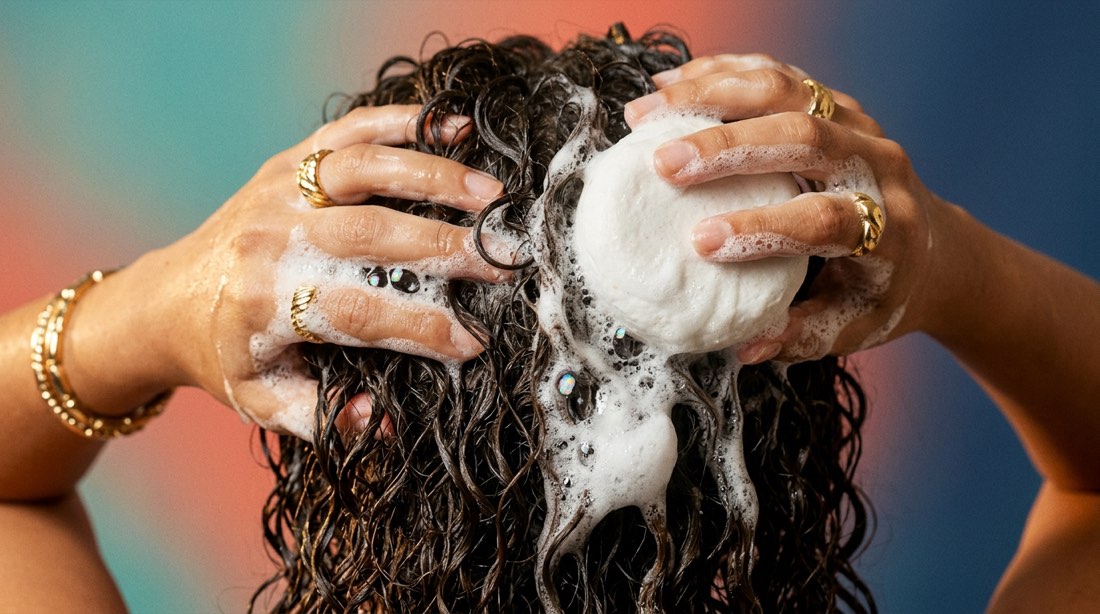 Hands working a shampoo bar into wet curly hair